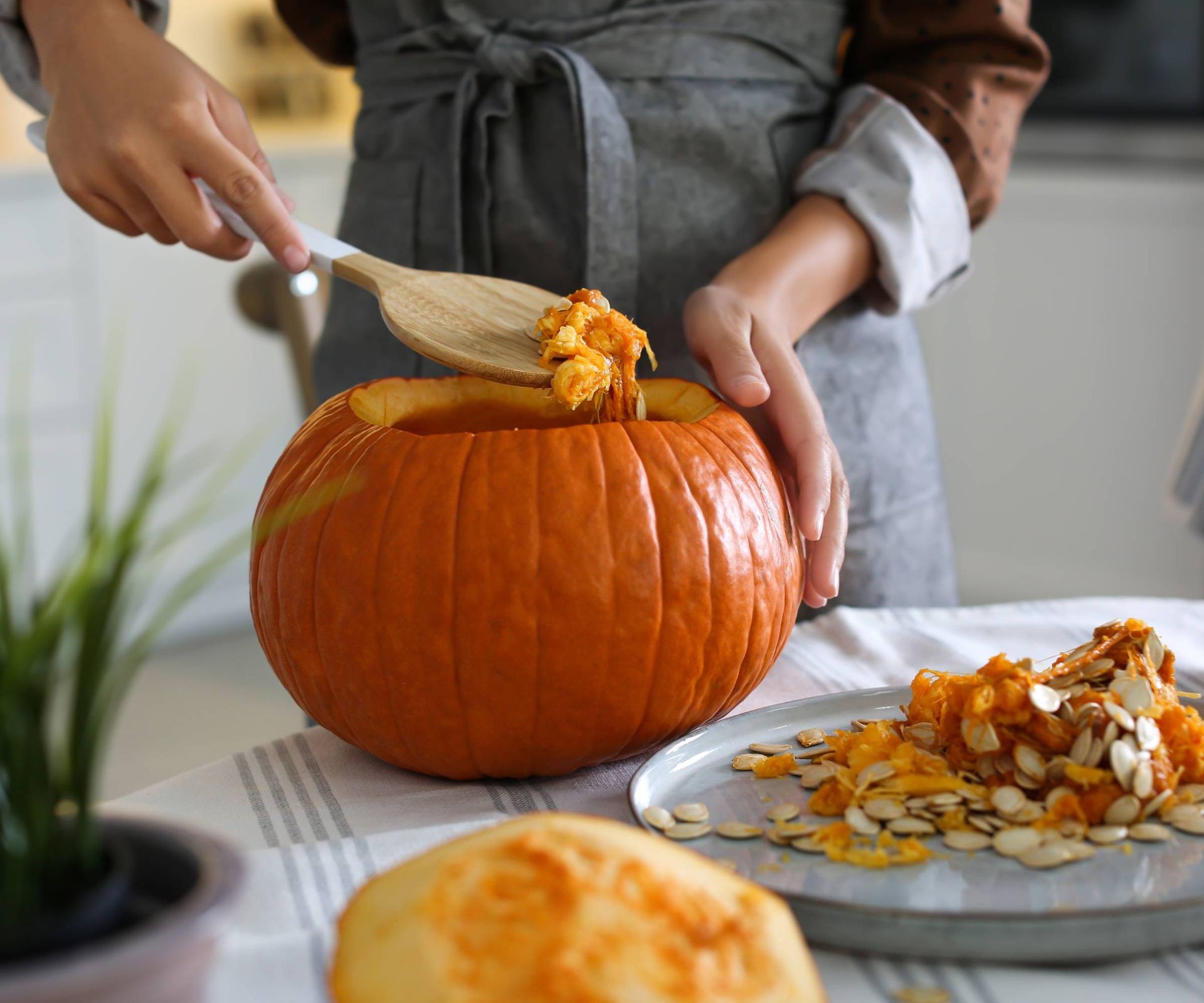 A person uses a wooden spoon to scoop out pumpkin seeds and pulp from inside a carved pumpkin.