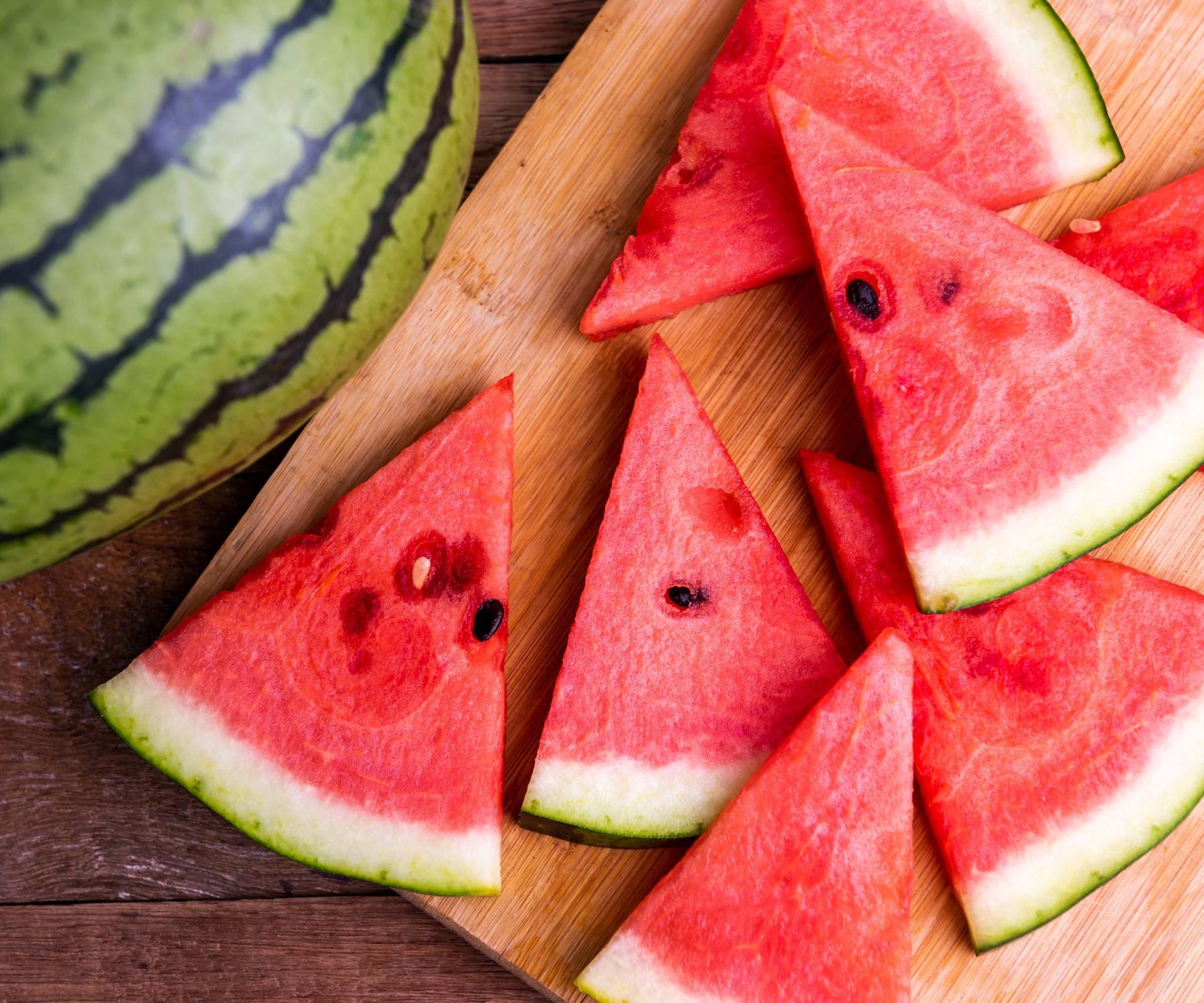 Brightly colored watermelon slices on a cutting board next to a whole melon