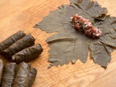 Hands holding large, healthy grape leaves used for wrapping food