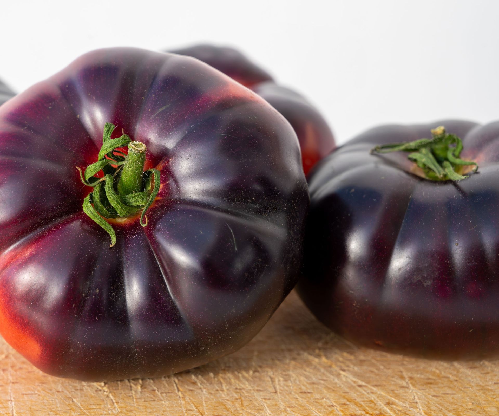 Pile of freshly harvested Purple Calabash tomatoes, showcasing their irregular, ruffled shapes and rich purple-chocolate colors.