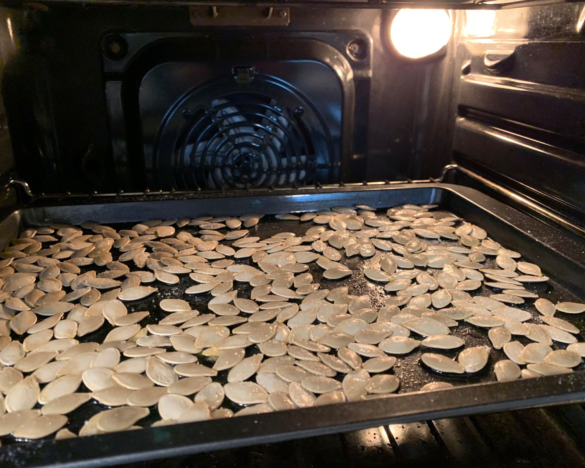 Pumpkin seeds roasting on a baking sheet in an oven