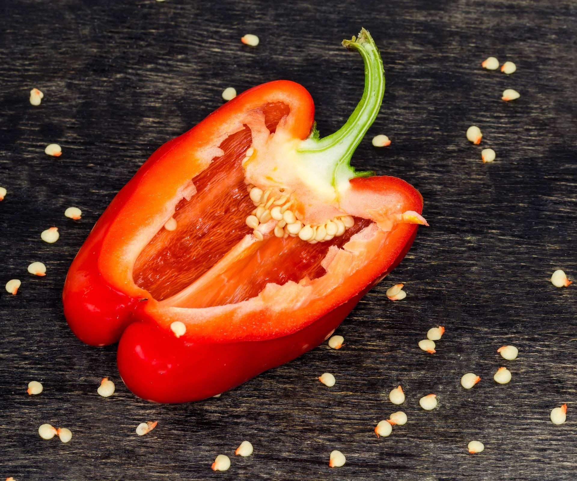 Ripe red bell pepper cut in half revealing seeds inside, placed on a wooden surface.