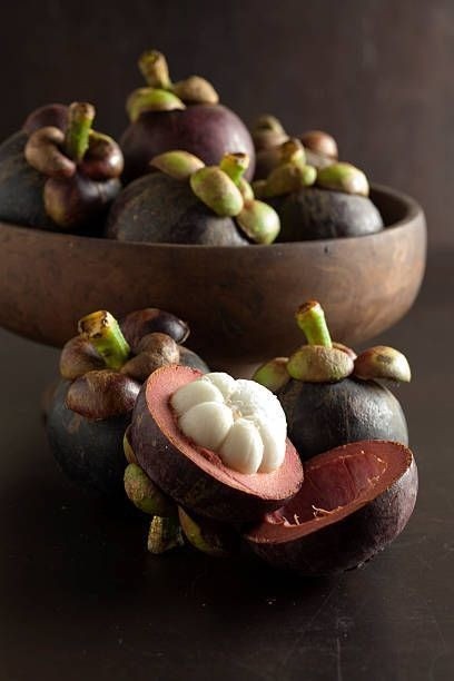 Several dark purple mangosteen fruits with green calyxes