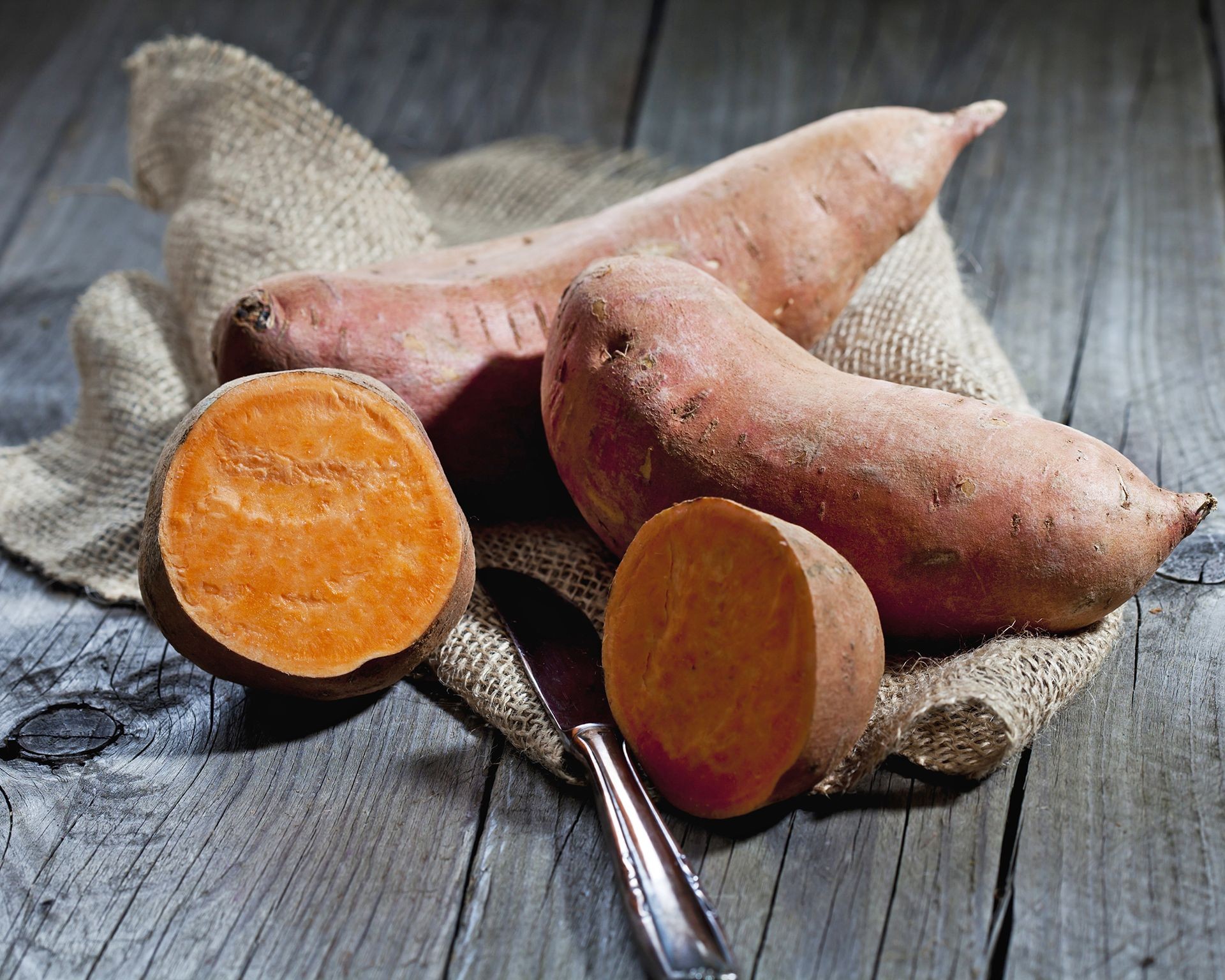 Several harvested sweet potatoes, including orange and purple varieties, displayed on a wooden table